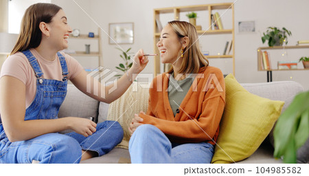 Women friends, makeup and lipstick while happy on home sofa and talking about product on lips. Females or sisters relax on living room couch for funny conversation about cosmetics and beauty 104985582