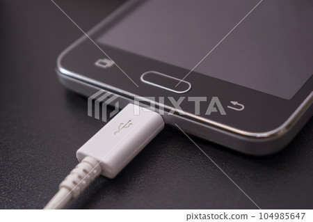 black smartphone on black background with white cable black smartphone on black background with white cable 104985647