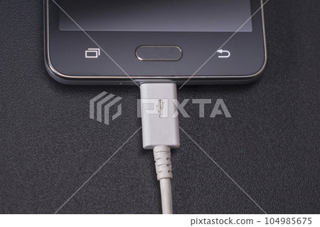 black smartphone on black background with white cable 104985675