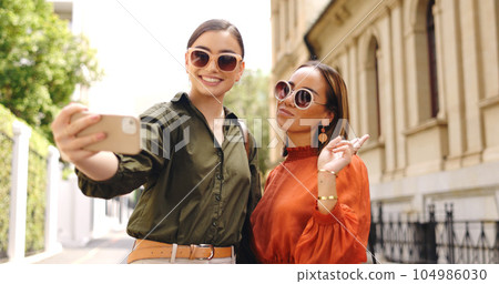 Phone, selfie and friends outdoor taking a profile picture together for social media. Digital, women and girl friend in a home with peace sign posing on a mobile for web app. Phone, selfie and friends outdoor taking a profile picture together for social media. Digital, women and girl friend in a home with peace sign posing on a mobile for web app. 104986030