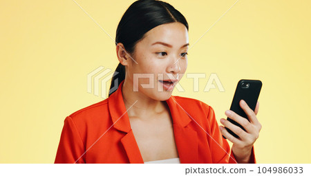 Winner, success celebration and Asian woman with phone in studio isolated on a yellow background. Surprise, fist pump or happy female with mobile to celebrate after winning lottery prize or good news 104986033