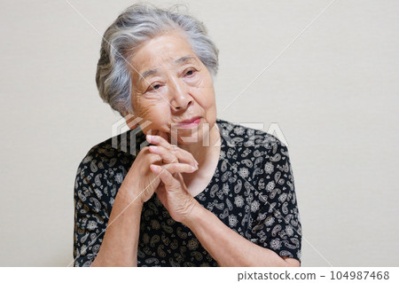 An elderly woman thinking with her hands folded An elderly woman thinking with her hands folded 104987468