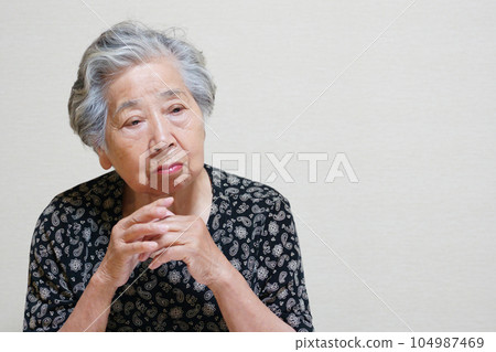An elderly woman thinking with her hands folded An elderly woman thinking with her hands folded 104987469