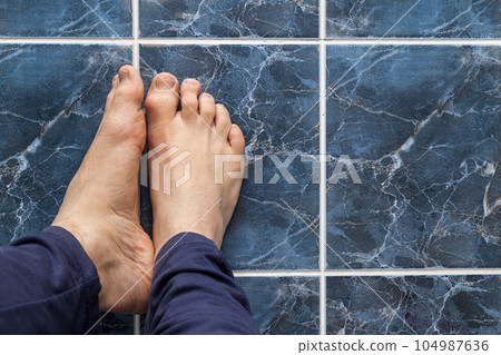 Young man crossing feet on square tiles. Veins in feet visible. Young man crossing feet on square tiles. Veins in feet visible. 104987636