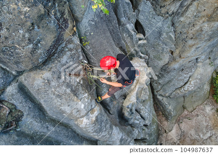 Young man climbing steep wall of rocky mountain. Male climber overcomes challenging route. Engaging in extreme sport concept. 104987637