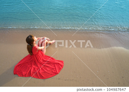 Young happy woman wearing red dress resting on sea beach enjoying warm summer morning. Young happy woman wearing red dress resting on sea beach enjoying warm summer morning. 104987647