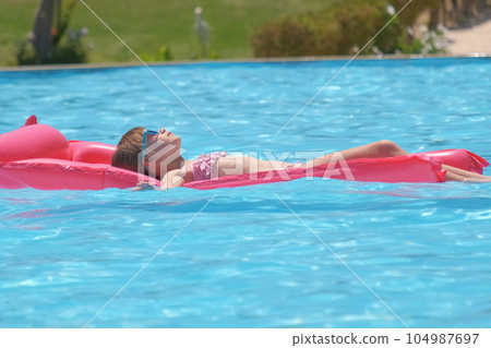 Young child girl relaxing on summer sun swimming on inflatable air mattress in swimming pool during tropical vacations. Summertime activities concept 104987697