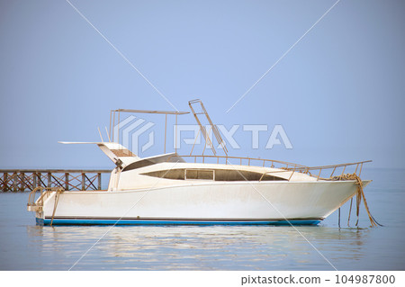 White motor boat floats in ocean water at long pier bridge under bright blue sky, view from sandy beach. Summer traveling concept White motor boat floats in ocean water at long pier bridge under bright blue sky, view from sandy beach. Summer traveling concept 104987800