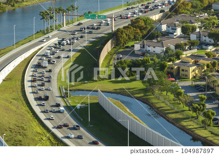 View from above of apartment residential condos near noisy highway road with car traffic in Miami suburban area. American condominiums as example of real estate development in USA suburbs View from above of apartment residential condos near noisy highway road with car traffic in Miami suburban area. American condominiums as example of real estate development in USA suburbs 104987897