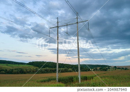 Tower with electric power lines for transfering high voltage electricity located in agricultural cornfield. Delivery of electrical energy concept. 104987940