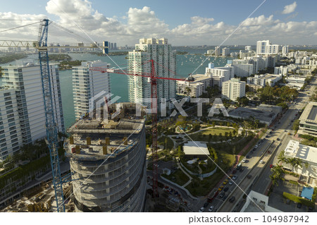 Tower lifting cranes at high residential apartment building construction site. Real estate development in Miami urban area Tower lifting cranes at high residential apartment building construction site. Real estate development in Miami urban area 104987942