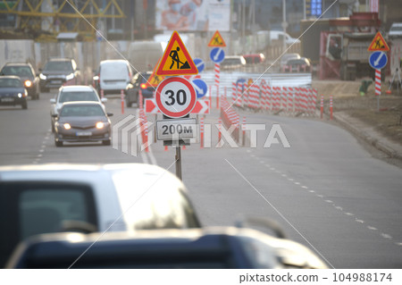 Roadworks warning traffic signs of construction work on city street and slowly moving cars 104988174