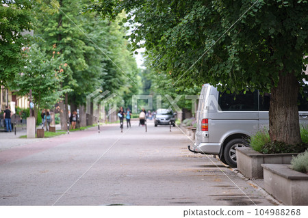 Passenger van car parked on a city alley street side with blurred walking pedestrians Passenger van car parked on a city alley street side with blurred walking pedestrians 104988268