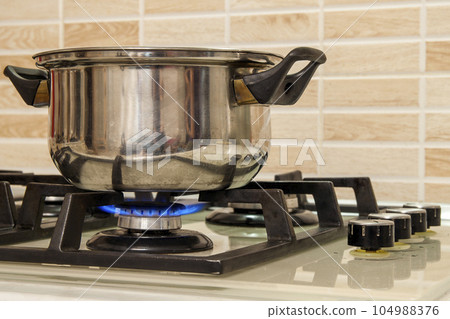 Metal cooking pot standing on kitchen stove with flame. 104988376