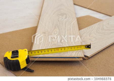 Measuring tape on laminate floor plank 104988378