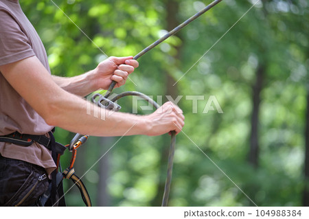 Man belays his partner climber with belaying device and rope. Climber's handsman holding equipment for rock mountaineering security. 104988384