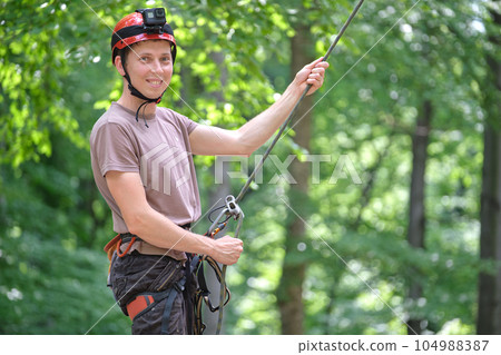 Man belays his partner climber with belaying device and rope. Climber's handsman holding equipment for rock mountaineering security. Man belays his partner climber with belaying device and rope. Climber's handsman holding equipment for rock mountaineering security. 104988387