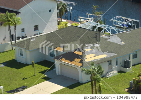 Hurricane Ian destroyed house roof in Florida residential area. Natural disaster and its consequences 104988472