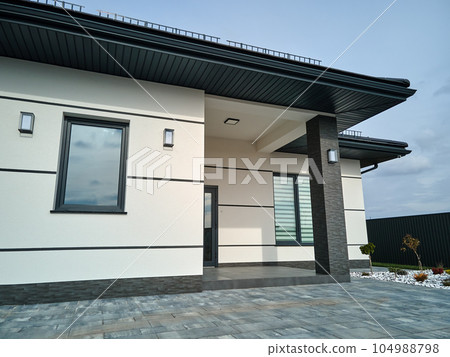 Exterior of modern contemporary comfortable house with front porch, stylish door, paved yard and shuttered windows Exterior of modern contemporary comfortable house with front porch, stylish door, paved yard and shuttered windows 104988798