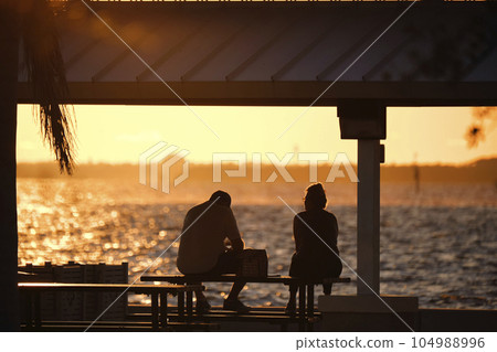 Dark silhouette of people resting under alcove roof on sea shore in public park at sunset 104988996