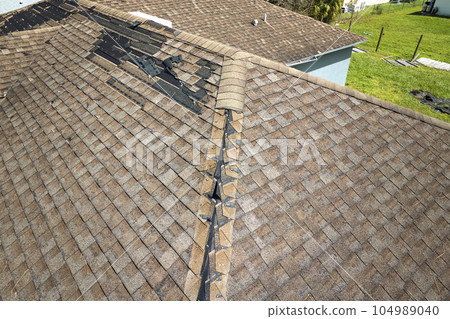 Damaged house roof with missing shingles after hurricane Ian in Florida. Consequences of natural disaster Damaged house roof with missing shingles after hurricane Ian in Florida. Consequences of natural disaster 104989040