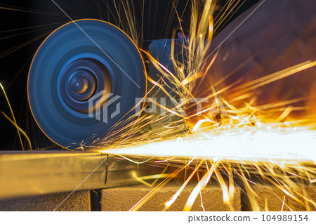 Close-up of worker hands cutting metal with grinder. Sparks while grinding iron. Low depth of focus 104989154