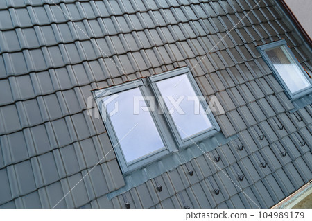 Closeup of attic window on house roof top covered with ceramic shingles. Tiled covering of building 104989179
