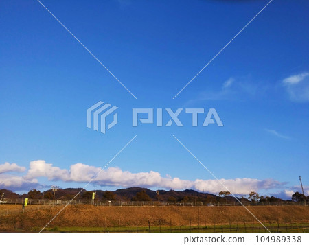 Rural landscape with clear blue sky and white clouds just above the mountains 104989338
