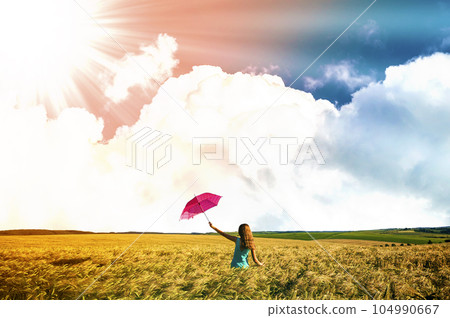 Beauty young girl outdoors enjoying nature. Beautiful teenage model girl in blue dress with red umbrella on the wheat field in rays of sun light. 104990667