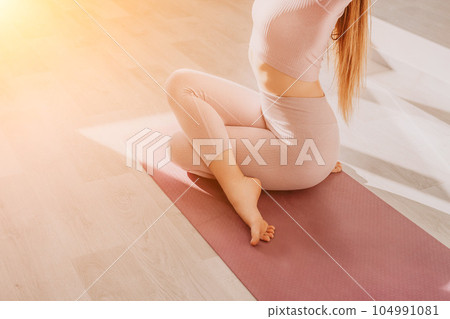 Young sporty woman, fitness instructor in pink sportswear doing stretching and pilates on yoga mat in the studio with mirror. Female fitness yoga routine concept. Healthy lifestyle and harmony. 104991081