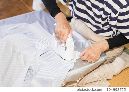 Senior woman ironing cutter shirt with clothing steamer Senior woman ironing cutter shirt with clothing steamer 104992755