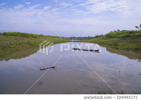 Canal with green grass and vegetation reflected in the water nearby Padma River in Bangladesh Canal with green grass and vegetation reflected in the water nearby Padma River in Bangladesh 104993172