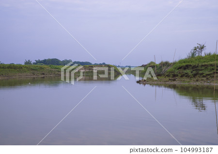 Canal with green grass and vegetation reflected in the water nearby Padma River in Bangladesh  104993187