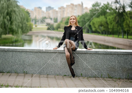 Pretty woman sitting on river bank in city park near her office 104994016