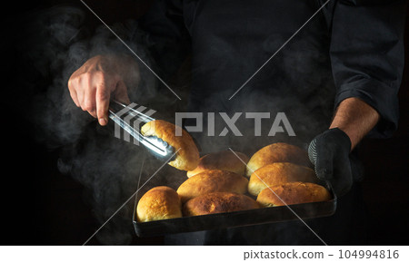 The baker is baking pies or buns on a hot baking sheet. Black space for menu or recipe. Ukrainian national dish 104994816