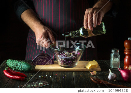 The cook adds oil to the red cabbage salad. Cooking a delicious vegan dish with the hands of a chef in the kitchen. Menu idea for hotel or restaurant 104994828