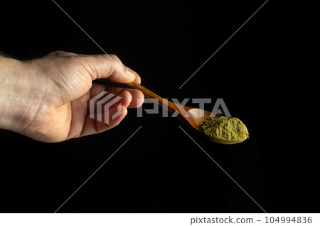 Mixture of dry ground herbs in a wooden spoon in a person hand before adding to tea. Free space for advertising on a black background. 104994836