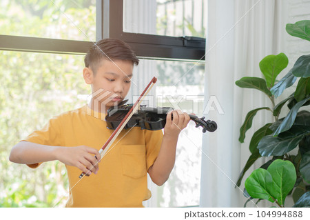 A Little Asian kid playing and practice violin musical string instrument against in home, Concept of Musical education, Inspiration, Teenager art school student. 104994888