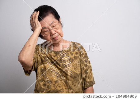 A senior woman who has a severe headache suffers from a stroke ,brain disease,patient holding head with her hand,suffering from senile dementia,memory disorders, confused old elderly with Alzheimer 104994909