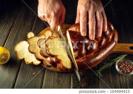 Slicing delicious fresh bread or kalach before dinner by the chef's hands. Healthy food or delicatessen concept Slicing delicious fresh bread or kalach before dinner by the chef's hands. Healthy food or delicatessen concept 104994915