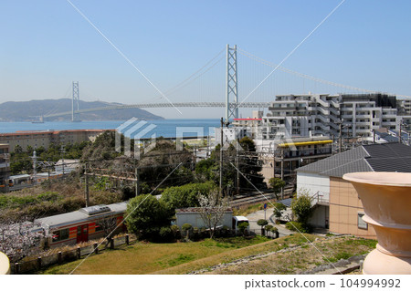 View of the Akashi Kaikyo Bridge from the Goshikizuka Tumulus over the Sanyo Electric Railway Series 6000 on the east side of Kasumigaoka Station on the Sanyo Electric Railway 104994992