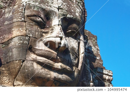 The art of ancient Cambodia represented by a stone face sculpture with a smile. The art of ancient Cambodia represented by a stone face sculpture with a smile. 104995474
