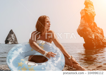 Woman summer sea. Happy woman swimming with inflatable donut on the beach in summer sunny day, surrounded by volcanic mountains. Summer vacation concept. Woman summer sea. Happy woman swimming with inflatable donut on the beach in summer sunny day, surrounded by volcanic mountains. Summer vacation concept. 104996112