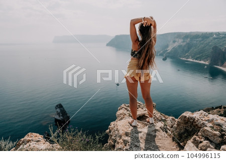 Woman travel sea. Happy tourist enjoy taking picture outdoors for memories. Woman traveler looks at the edge of the cliff on the sea bay of mountains, sharing travel adventure journey Woman travel sea. Happy tourist enjoy taking picture outdoors for memories. Woman traveler looks at the edge of the cliff on the sea bay of mountains, sharing travel adventure journey 104996115