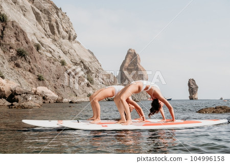 Woman sup yoga. Happy sporty woman practising yoga pilates on paddle sup surfboard. Female stretching doing workout on sea water. Modern individual female hipster outdoor summer sport activity. 104996158