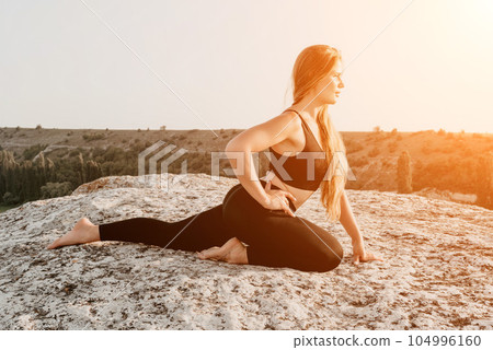 Fitness woman. Happy middle-aged fitness woman doing stretching and pilates on a rock near forest at sunset. Female fitness yoga routine. Healthy lifestyle with focus on well-being and relaxation. 104996160