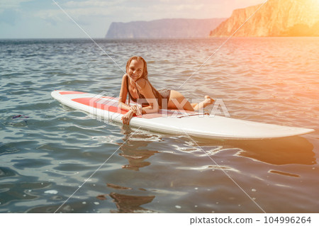 Woman sup sea. Sports girl on a surfboard in the sea on a sunny summer day. In a black bathing suit, he sits on a sapa in the sea. Rest on the sea. 104996264
