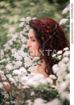 Woman spirea flowers. Portrait of a curly happy woman in a flowering bush with white spirea flowers. 104996266