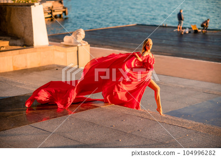 Sunrise red dress. A woman in a long red dress against the backdrop of sunrise, bright golden light of the sun's rays. The concept of femininity, harmony. 104996282