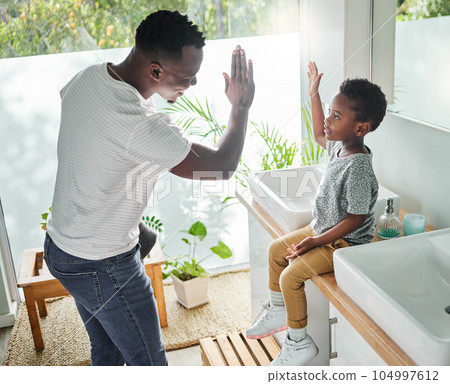 Encourage your child to follow good hygiene practices. High angle shot of a father giving his son a high five in a bathroom at home. 104997612